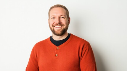 Fototapeta premium Smiling caucasian young adult male in orange sweater against white background