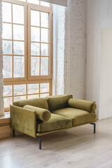 Cozy green khaki velours couch in bright and airy living space with large windows and white brick wall backround. Modern loft minimalist design of interior, living space, home decor