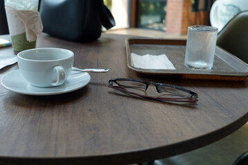 Coffee cup and eyeglasses on table in coffee shop