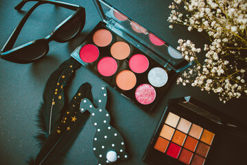Eyeshadow palettes, flowers, glasses, rabbit, feathers and flowers on black paper background