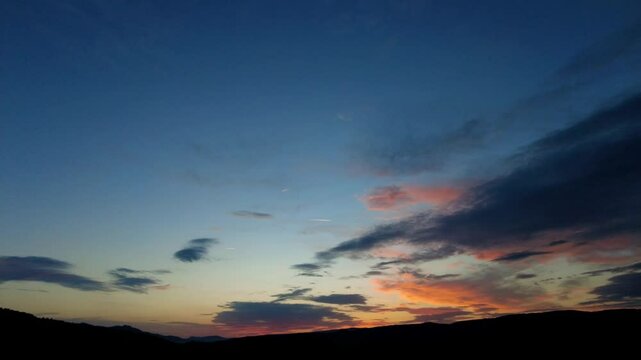 Majestic sunset sky transforming with moving clouds over dark hills