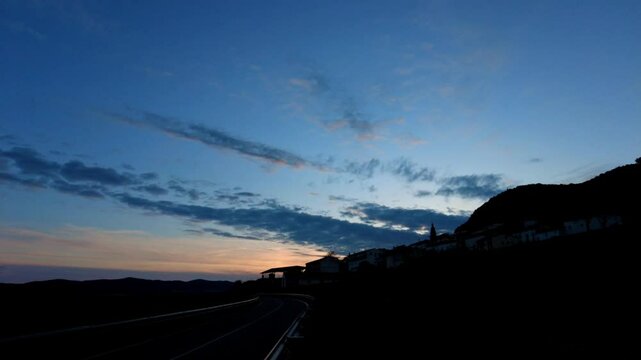 Airplane contrail forming over a small hilltop village at sunset