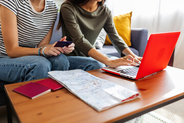 Two young female friends booking online their vacation trip, doing a reservation of their...