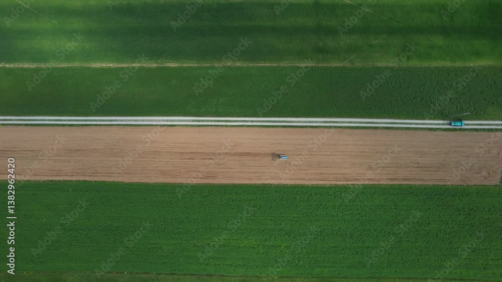Poster aerial footage capturing farmer operating small crawler tractor, creating contrasting geometric patt