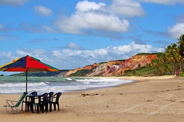 Beach near Joao Pessoa city, Paraiba state, northeast of Brazil. Parasol and chairs on the empty beach, waves crashing on the water's edge and multi-colored hills