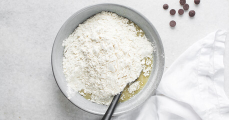 Overhead view of flour being folded into cookie dough, top view of cookie dough being mixed in a grey bowl, process of making cookie dough or chocolate chip cookie dough