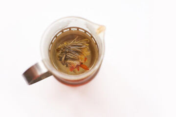 Blooming flower tea in glass teapot on white background with herbal infusion.
