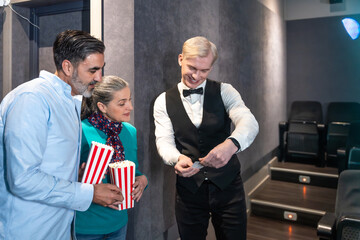 Usher checking tickets of couple entering movie theater with popcorn