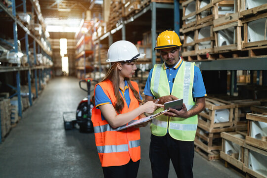 asian male and female worker checking storage. male and female team inspect shelf stock safety protection like teamwork. man and woman cargo support in workplace looking screen and write list board