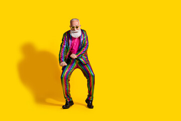 Colorful elegant senior man dancing happily against a vibrant yellow background in stylish suit