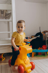 Little boy sitting sitting on toy yellow horse in kinder room. Happy smiling child playing at home