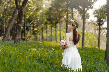 A girl in white dress holding flowers standing among the grass