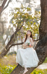 A girl in white dress sits on a tree holding flowers and feels the sunshine