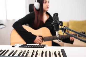 Beautiful Asian teen girl playing guitar, composing music in home recording studio using computer,...