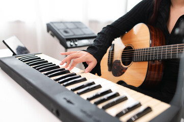 Beautiful Asian teen girl playing guitar, composing music in home recording studio using computer,...