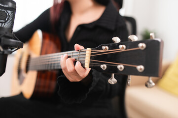 Beautiful Asian teen girl playing guitar, composing music in home recording studio using computer,...