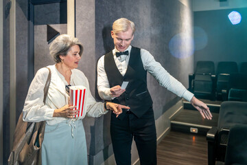 Usher showing seat to woman holding popcorn bucket in movie theater