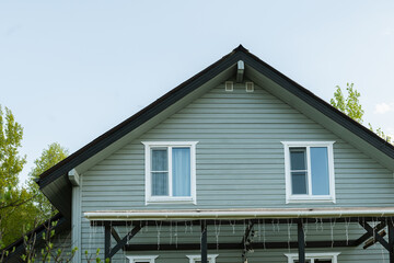 Front view, second floor of contemporary house facade showcasing gray siding, roof and symmetrical windows. Summer. Contemporary house of timber with garland decorated patio. Outdoors.