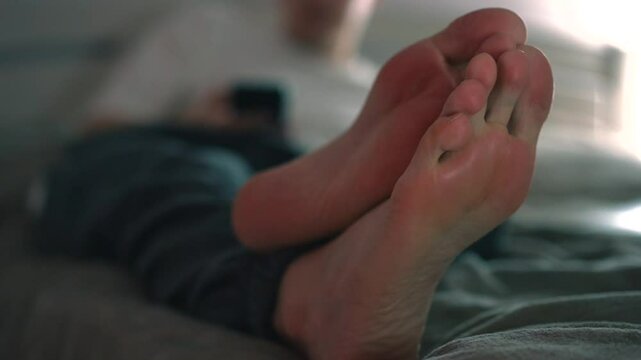 Un jeune homme est allong&eacute; sur un lit avec un t&eacute;l&eacute;phone dans les mains.
Un homme clique sur un smartphone alors qu'il est allong&eacute; sur un lit dans une chambre.