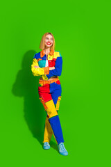 Young woman in vibrant multicolored outfit against green vertical background, smiling confidently and posing gracefully