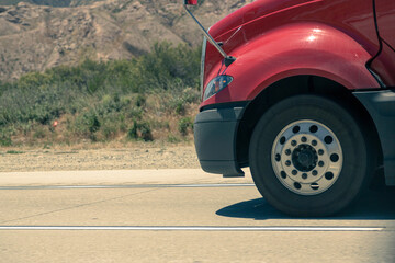 Commercial truck wheel rotating on paved road surface. Heavy-duty truck wheel rolling on highway. Large freight vehicle tire in motion detail. Red vehicle cab partially shown. Cargo transport sector.