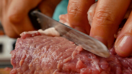 A woman cuts red pork meat into pieces. Cooking meat dishes.