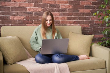 Young caucasian female adult relaxing on sofa with laptop in cozy home environment.