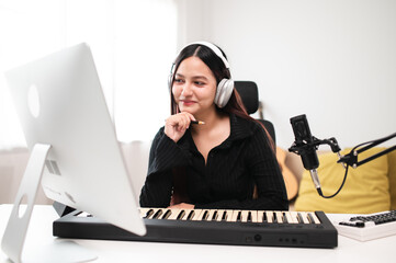 Beautiful Asian teen girl playing guitar, composing music in home recording studio using computer,...