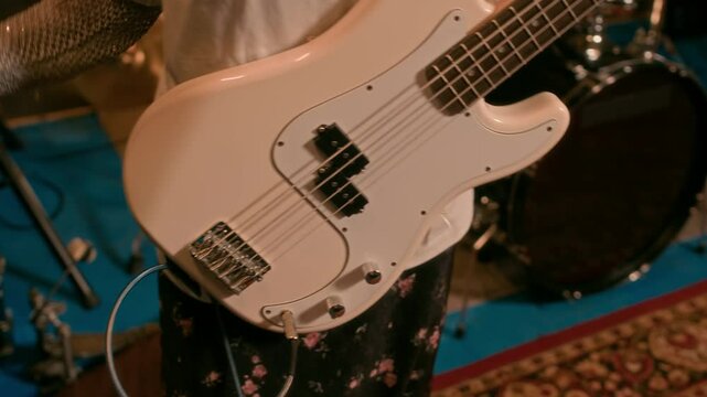 Close-up shot of unrecognizable person connecting white electric bass guitar to amplifier, preparing for performance in music studio