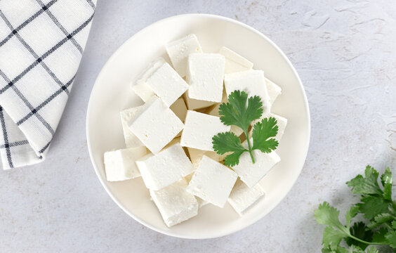 Cubes of traditional Indian paneer cheese made from fresh milk and lemon with cilantro on white background. Top view.
