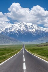 Fototapeta premium Scenic Road Leading to Majestic Snow Capped Mountain Under Blue Sky with Fluffy Clouds in Summer