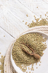 Plate full of dried raw green lentils with a wooden scoop on white table top view. Vegetarian food