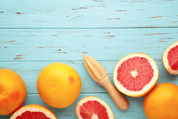 Fresh organic grapefruit and a wooden juicer on blue wooden background, top view.