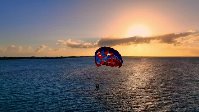 Two people parasailing over the sea waters at sunset, capturing the colors of a Caribbean evening