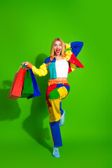Vibrant young woman holds colorful shopping bags on green background, showcasing cheerful energy and trendy fashion.