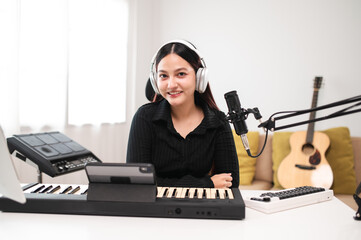 Beautiful Asian teen girl playing guitar, composing music in home recording studio using computer,...