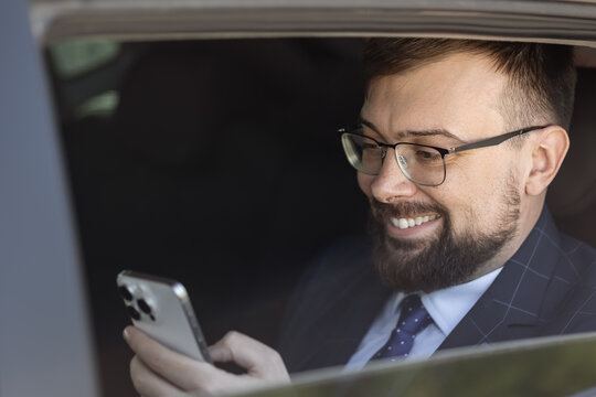 businessman with in car checking his phone. Dressed in a suit he smiles concentrating on the screen. professional demeanor. concert: using a phone while riding in taxi. traffic jam. business trip
