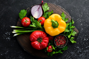 Assortment of fresh vegetables lies on a black background, tomatoes, pepper, onion, parsley, lemon. Top view.