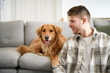 Portrait of a young man on the livingroom with golden retriever dog indoors at home.