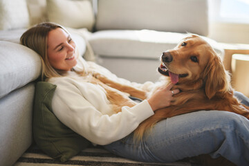 Portrait of a young woman on the livingroom with golden retriever dog indoors at home.