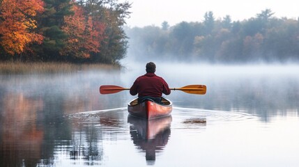 Man canoeing on misty lake during autumn season