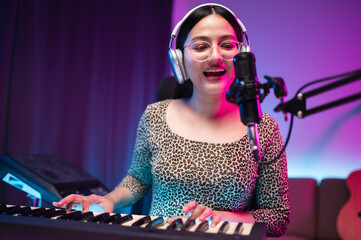 Asian teen girl playing guitar, composing music in home recording studio, LED lighting, at night using computer, headphones, condenser microphone, tablet and keyboard for mixing and mastering music.