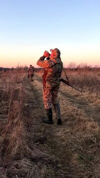 Hunter with duck call while hunting a wild bird. Hunter with gun, rifle on hunting. Hunter during duck hunting. Hunter shoots the birds of goose in sky. Dusk hunt on sunset. Calling ducks. Vertical