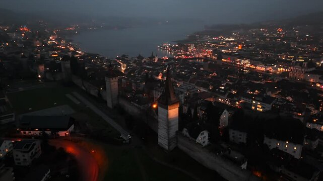Musegg Wall and its nine towers aerial view at night overlooking glowing city in Lucerne, Switzerland. Medieval defenses of Lucerne. Museggmauer Luzern und ihre neun Tuerme Luftaufnahme bei Nacht. 