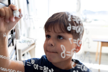 The child writes mathematical formulas on the glass with a marker.