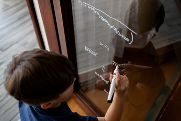 The child writes mathematical formulas on the glass with a marker.
