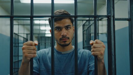 A person confined in a prison cell, with hands gripping the bars