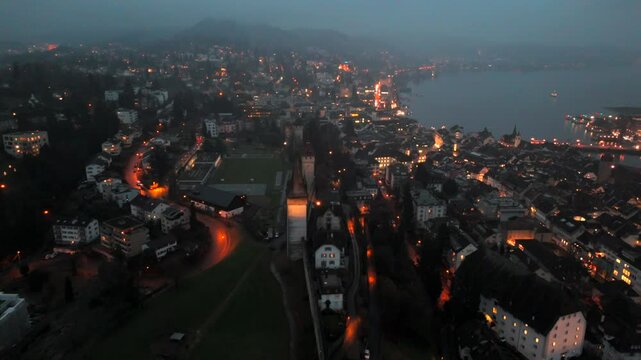 Musegg Wall and its nine towers aerial view at night overlooking glowing city in Lucerne, Switzerland. Medieval defenses of Lucerne. Museggmauer Luzern und ihre neun Tuerme Luftaufnahme bei Nacht. 