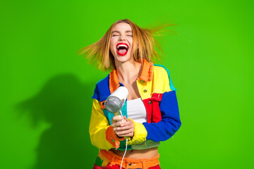 Vibrant young woman with colorful attire holding a hairdryer against a vivid green background, exuding joy and energy