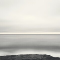 Fototapeta premium Serene seascape with smooth water under a cloudy sky creating a peaceful and minimalist atmosphere with a dark rock formation in foreground